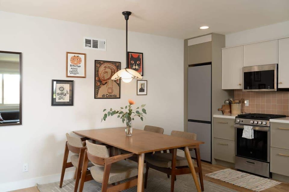 This inviting dining space features a warm wood table, comfortable seating, curated wall art, and a modern kitchen backdrop perfect for shared meals and relaxed evenings at home