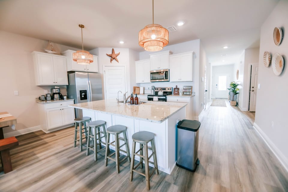 Step into this spacious, bright, and beautifully designed kitchen, the heart of the home! Featuring a large island with seating for four, stainless steel appliances, and elegant white cabinetry, this space is perfect for cooking, dining, and making memories.

Warm coastal touches, including woven pendant lighting and nautical decor, create a relaxing and inviting atmosphere. Th...