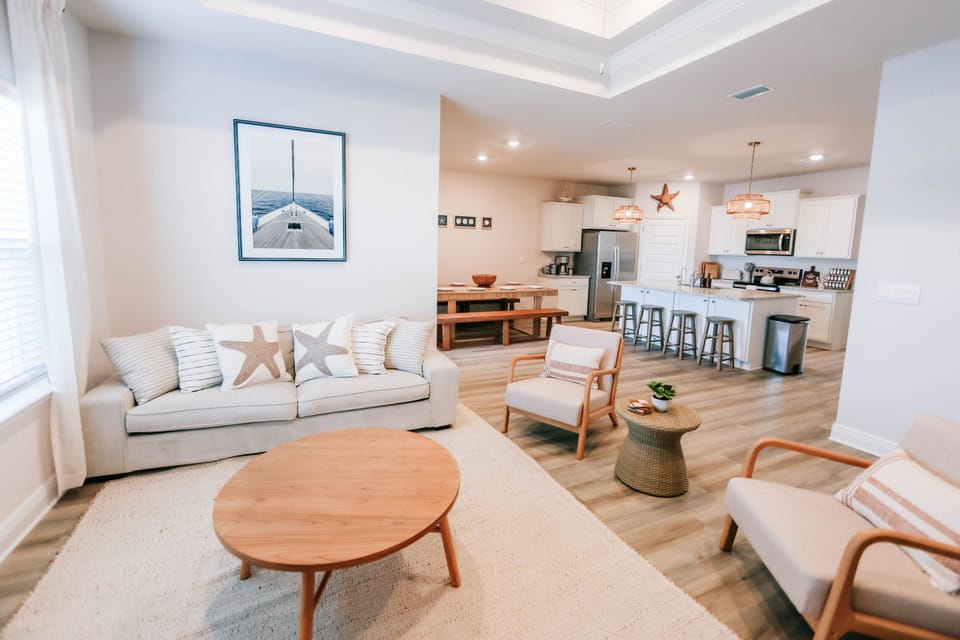 Welcome to this beautifully designed open-concept living space, where coastal charm meets modern comfort. Featuring a plush sofa adorned with nautical-themed pillows, cozy armchairs, and a sleek wooden coffee table, this space is perfect for gathering together and unwinding after a day of adventure.

Whether you're enjoying a movie night or sipping coffee in the morning, this c...