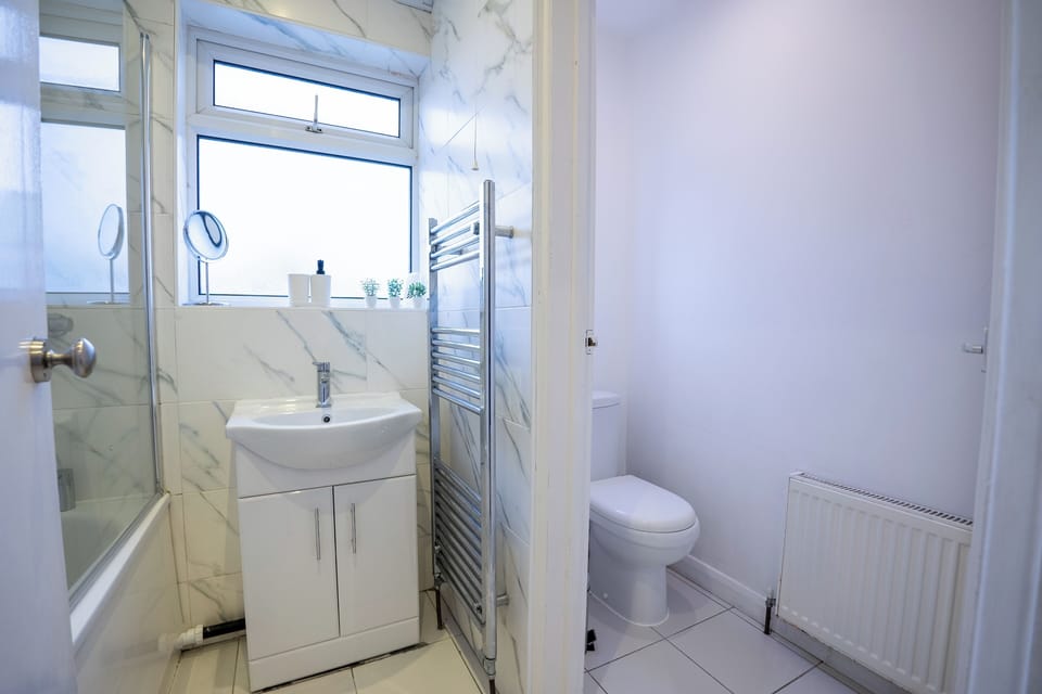 There is a bath with a shower, showergel, hand soap, towel dryer, mirror, toilet roll and toilet brush.