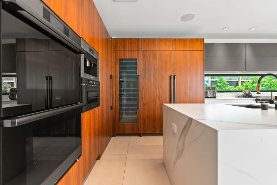 Sleek, wood-accented cabinetry blends with modern technology—note the wine fridge for your favorite vintage pairings.