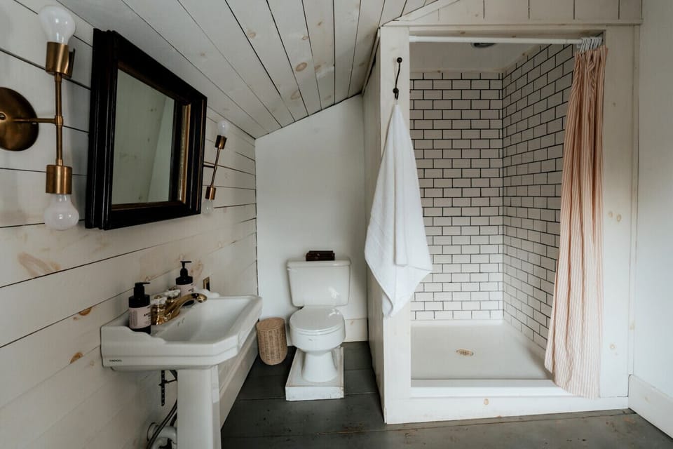 The Dickinson Room’s private ensuite bathroom combines vintage charm with modern comfort, featuring a classic subway-tiled shower, antique sink, and elegant brass fixtures.
