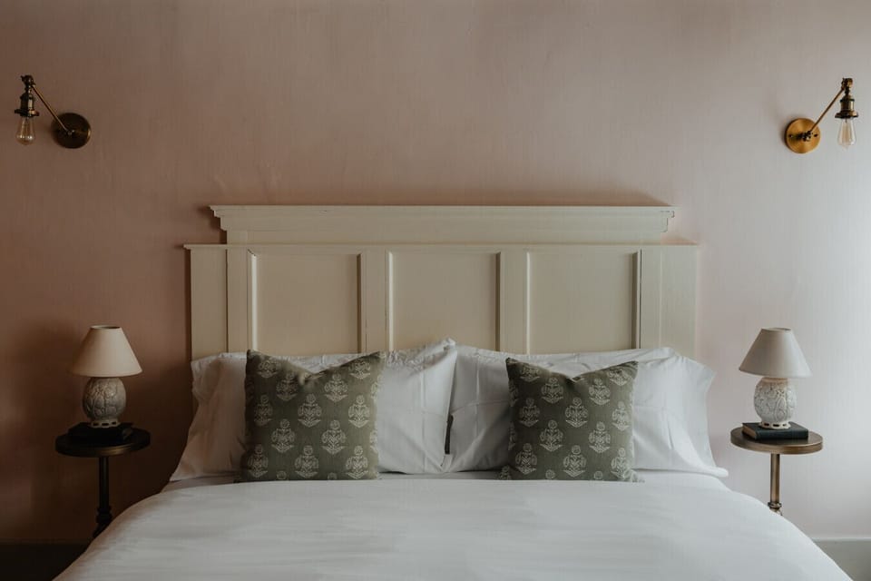 A serene and stylish retreat—the Fitzgerald Room’s king bed is framed by vintage wall sconces and soft textures, bringing warmth and sophistication to your stay.