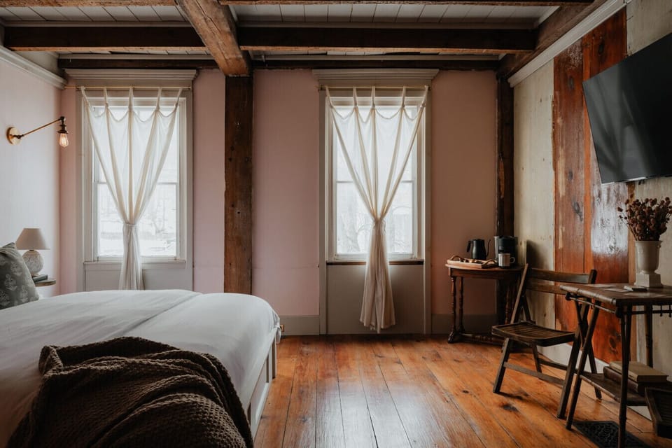 A grand and inviting space, the Fitzgerald Room boasts large windows, original wood beams, and a cozy king bed, embodying the charm and elegance of the Jazz Age.