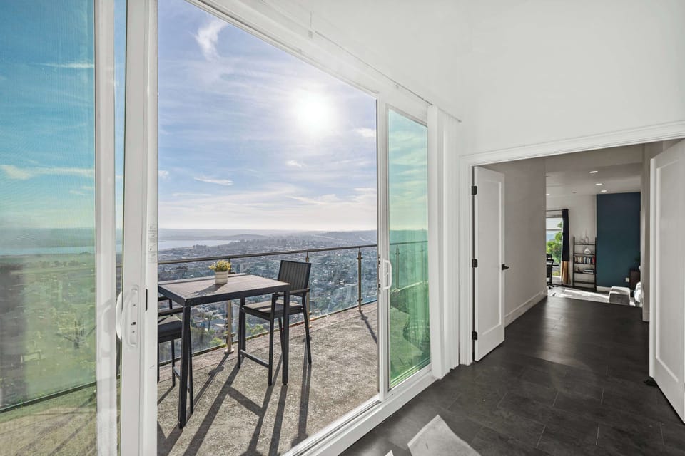 A breathtaking balcony with glass railings offers panoramic ocean and city views. Sliding doors bring in natural light, seamlessly connecting the indoor space to an outdoor dining area for a perfect retreat.