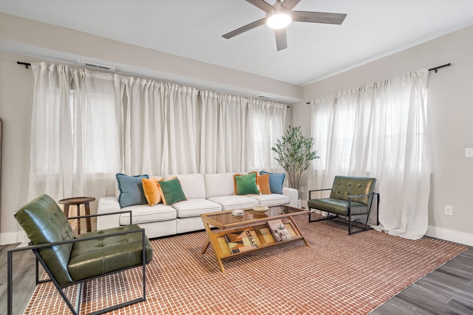 Modern living room with white sectional, bold accents, and natural light.
