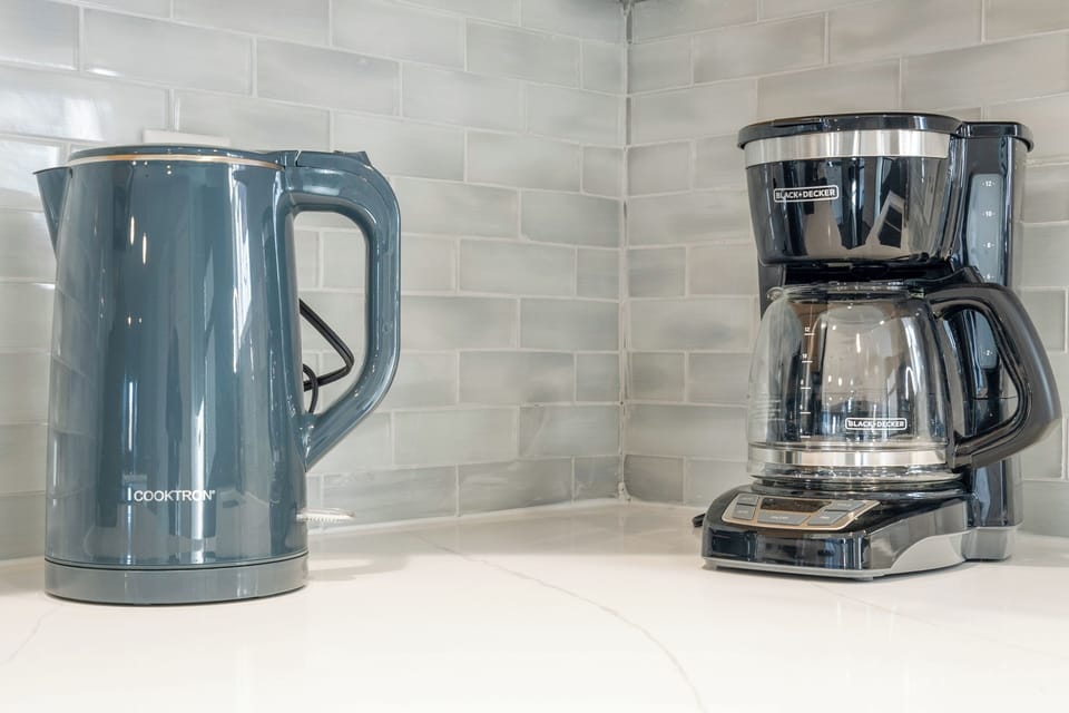 Coffee corner with kettle, drip maker, and glossy subway tile backsplash.
