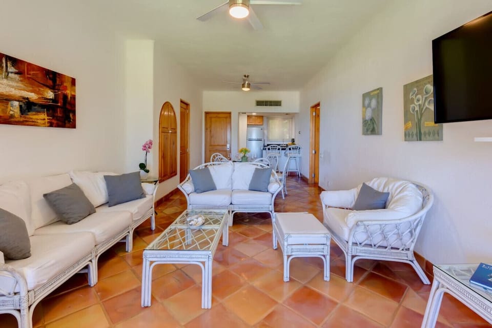 Living Room – Comfortable seating area with white wicker sofas and flat-screen TV.