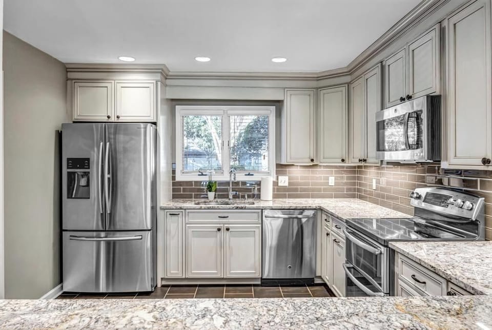 - Well appointed kitchen includes French door fridge, dishwasher, and window view
- Gorgeous granite counters and gray cabinets elevate the space with elegance
- Fully stocked for cooking, coffee, or entertaining with ease and charm