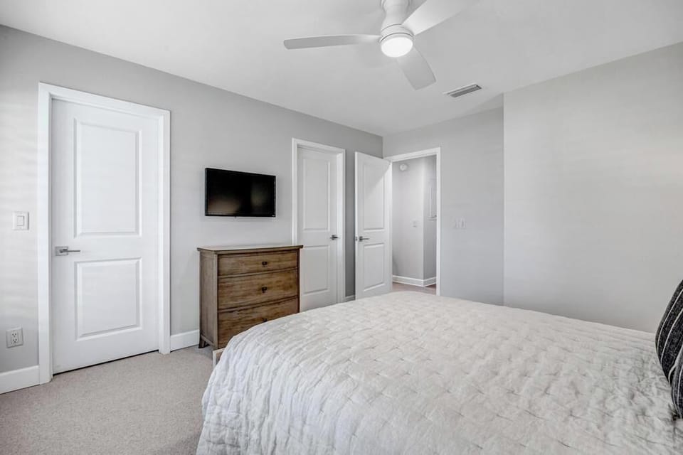 - Relax in this cozy queen room with a sleek wall mounted TV and wooden dresser
- Soft lighting, carpeted floors, and minimalist design offer a clean, peaceful vibe
- Two doors provide easy access to bathroom and hallway for convenience