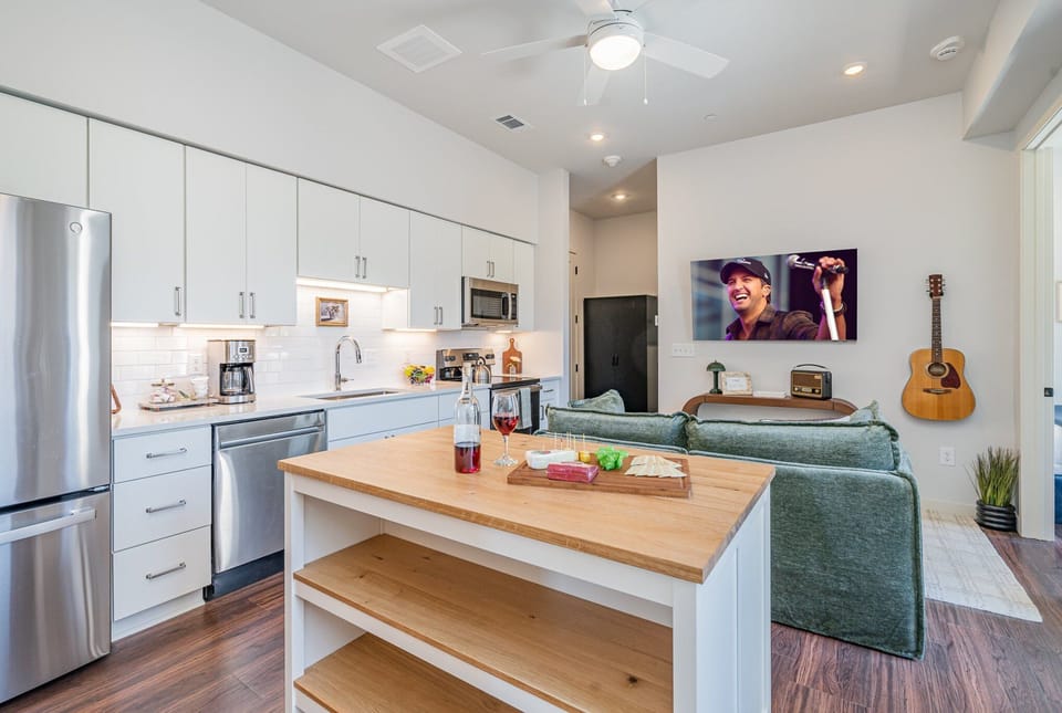 Kitchen with sleek white cabinetry, stainless steel appliances, and a butcher block island, perfect for preparing meals or enjoying a quick bite.