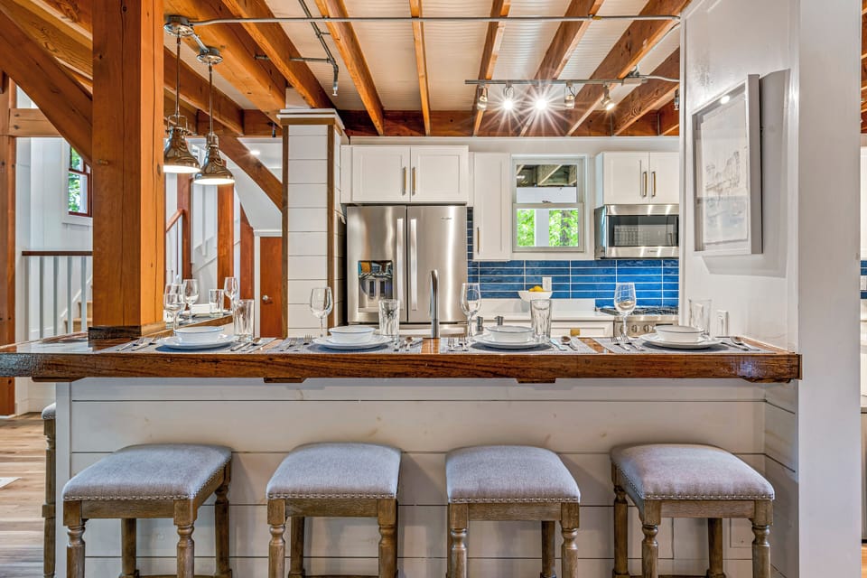 Kitchen with rustic bar, white cabinets, appliances, and stools.