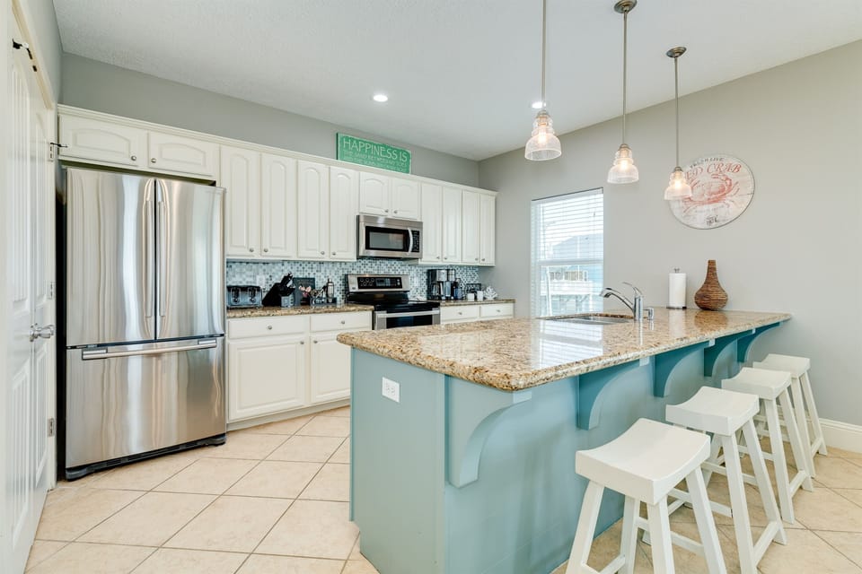 Bright, airy kitchen with granite island, stainless appliances, and cheerful beach accents—perfect for gathering, cooking, and casual dining.