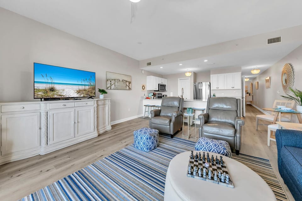 Relax in your bright, coastal-inspired living space with leather recliners facing a large TV, perfect for unwinding after beach days.