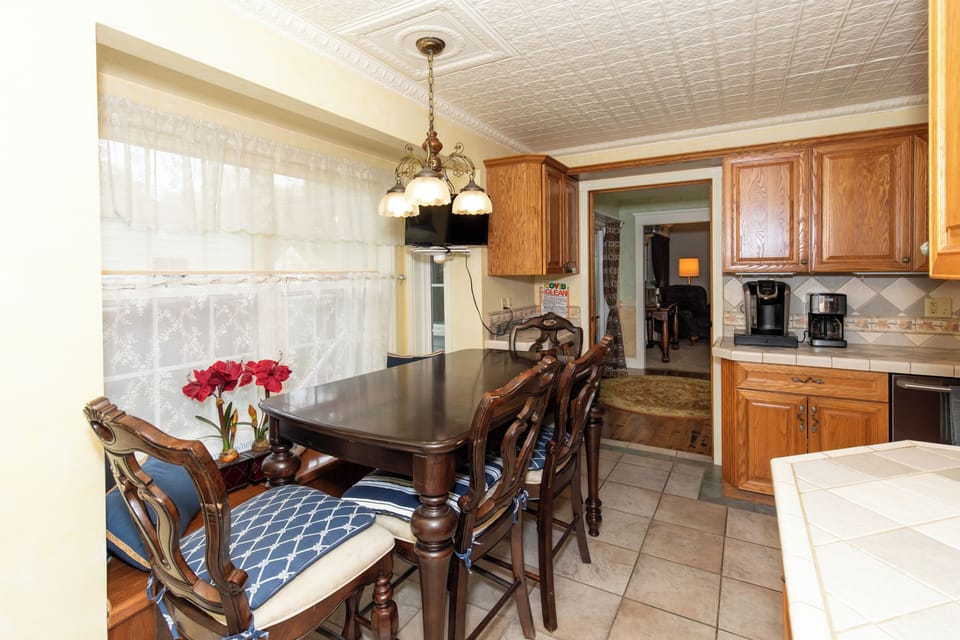 Your dining area features a classic dark wood table perfect for family meals, bathed in natural light from large windows. Decorative ceiling tiles and warm wood cabinetry create a homey, timeless charm.