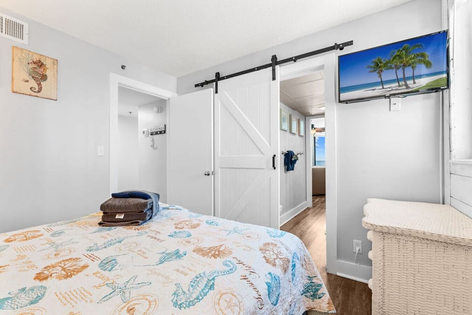 Unwind in the serene, beach-themed bedroom featuring a cozy queen-size bed and soft natural light.