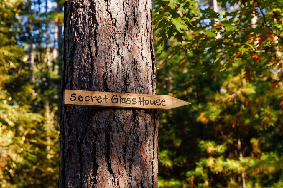 Follow the trail from the cabin | Spend the night or just the afternoon in the Secret Glass House | Open May-September only | Windows on 3-1/2 sides | Electricity, no heat | One double bed | New wicker chairs & table | Updated colors!