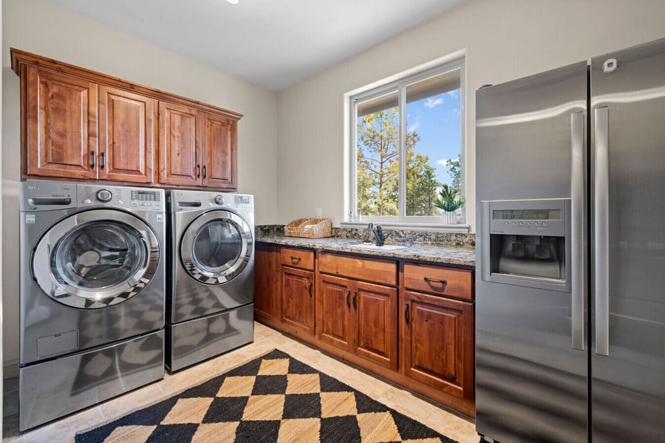 Even daily routines feel elevated in this thoughtfully designed laundry and utility room. Featuring high-efficiency washer and dryer, extra refrigerator space, and plenty of counter and cabinet storage—plus a view of the pines to make chores just a bit mo