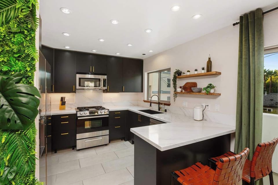 Cook in style in this modern kitchen! Featuring sleek black cabinetry, marble countertops, and stainless steel appliances, it’s perfect for home-cooked meals. A lush green accent wall adds charm, while an open layout keeps things airy.