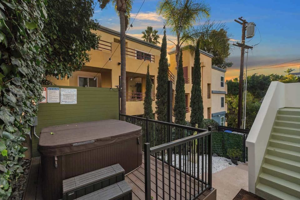 This cozy outdoor space features a private hot tub surrounded by lush greenery and modern railings.With warm lighting and a stylish backdrop of a contemporary building, it’s the perfect spot to unwind and enjoy a peaceful evening under the palm trees