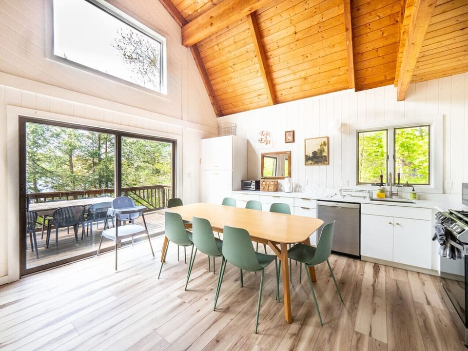 Full kitchen view with long dining table with seating for 8, green chairs, white cabinetry, stainless steel appliances, and open shelving.