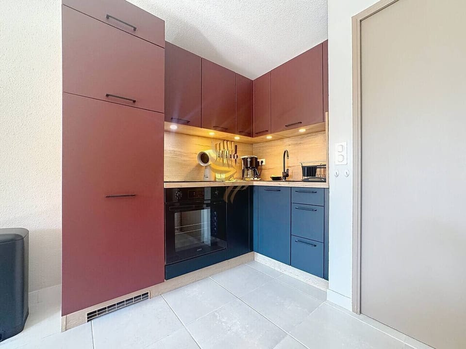La cuisine compacte mais bien équipée offre un espace fonctionnel avec des placards spacieux. Les couleurs sombres apportent une touche moderne et chic, parfaite pour les amateurs de design élégant.