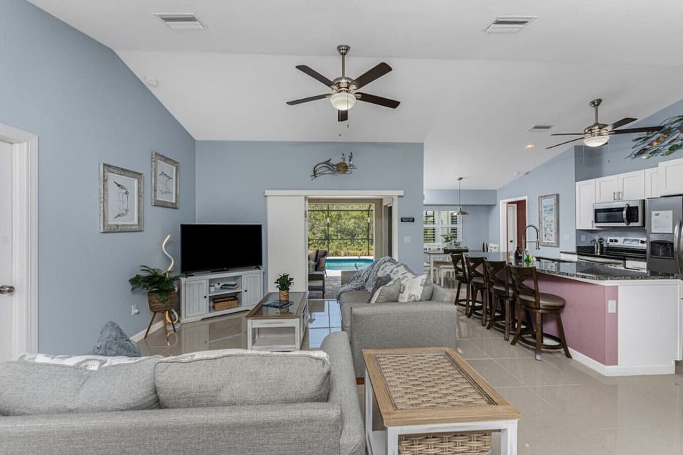 Open concept living space connecting the living room and kitchen, featuring vaulted ceilings, a smart Roku TV, comfortable seating including a sofa sleeper, and easy access to the private pool area.