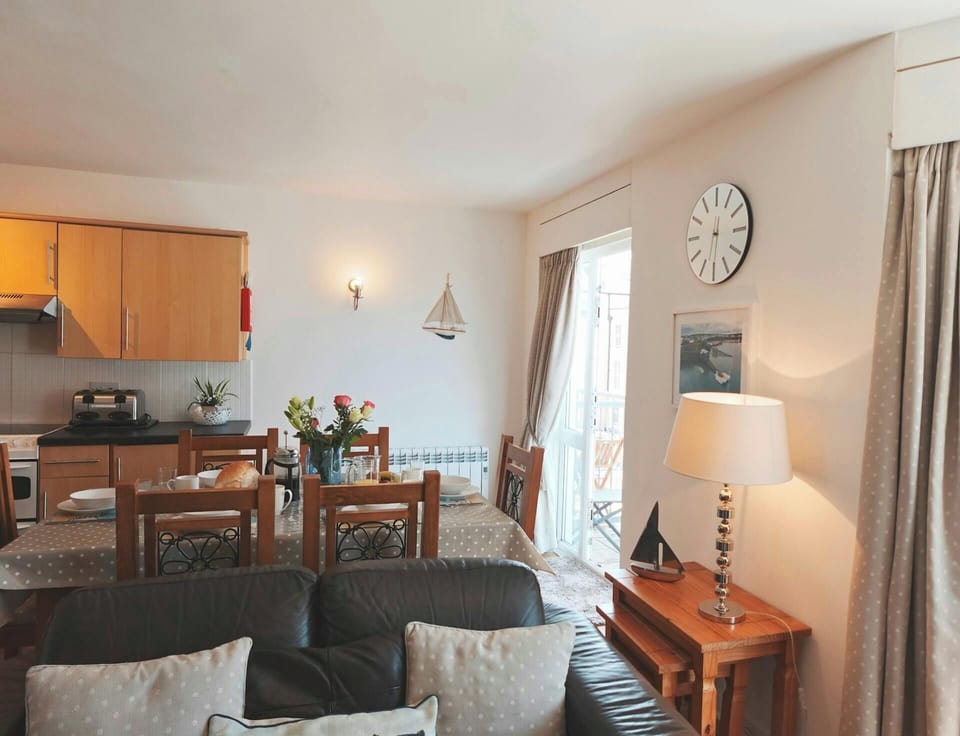 Dining table with wooden chairs beside a kitchenette with cupboards