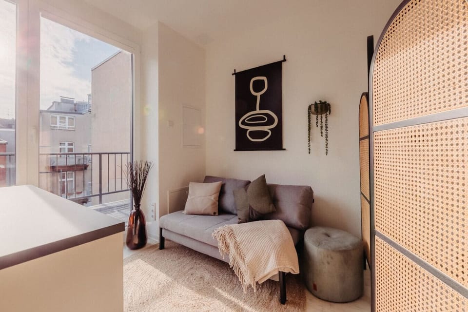 Die gemütliche Sitzecke mit modernem Sofa, stilvollen Kissen und einer weichen Decke lädt zum Entspannen ein. Das große Fenster sorgt für viel Licht und bietet einen schönen Blick auf die Umgebung. Eine harmonische Kombination aus Design und Komfort.
