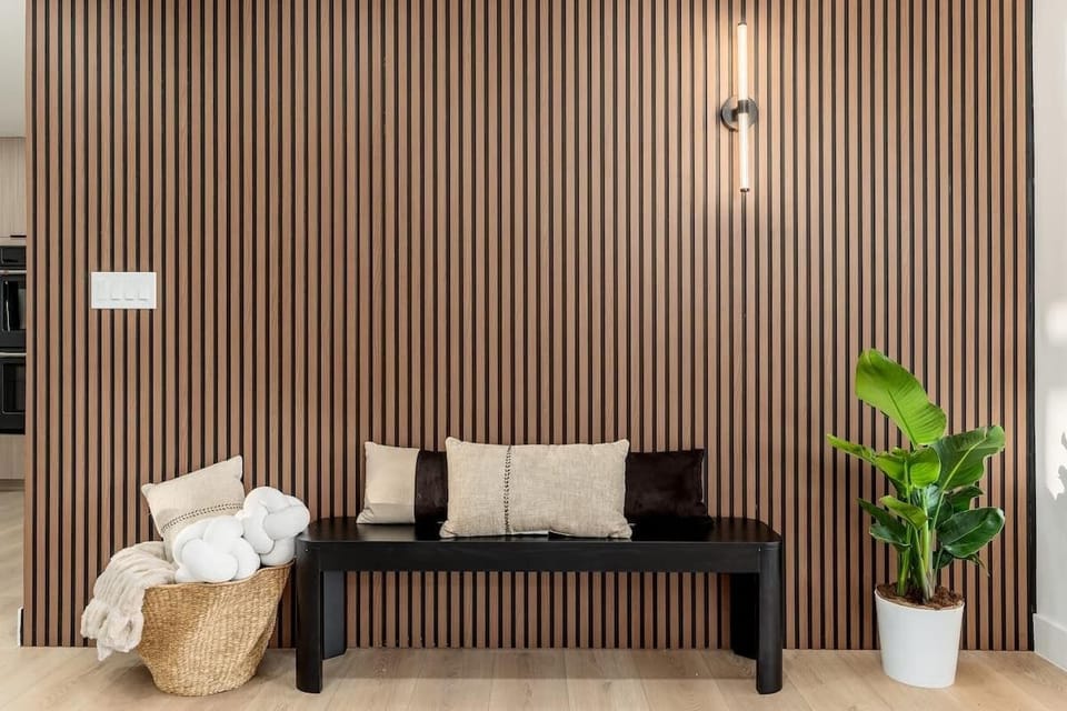 This stylish seating area features warm wood slat walls, modern lighting, and lush greenery—an inviting spot to unwind and feel at home.