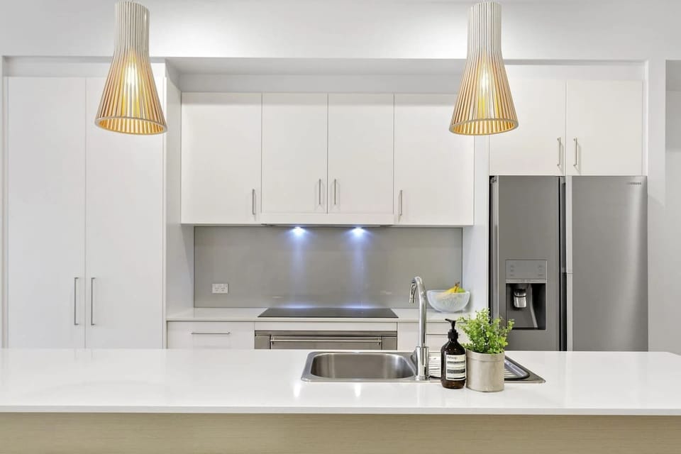 Modern kitchen setup with white cabinetry, stainless steel appliances, and elegant pendant lights above the countertop