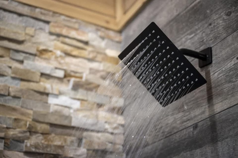 Indulge in a luxurious rinse under the rainfall showerhead, set against rich wood textures and stacked stone for a true spa-like escape.