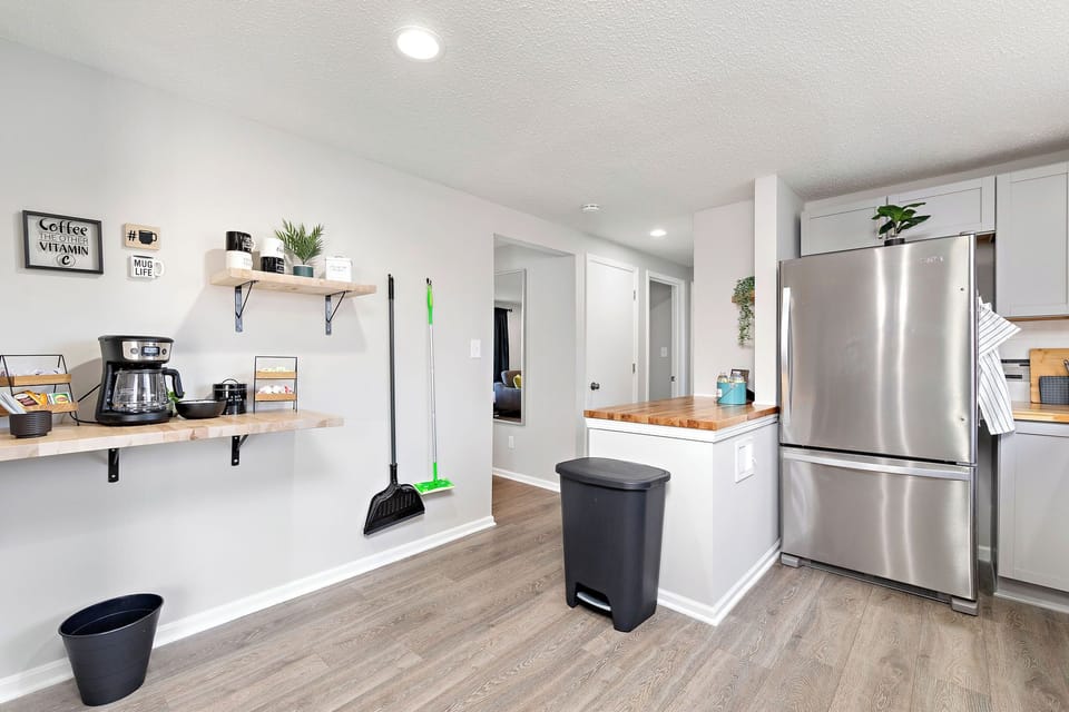 Modern kitchen with stainless steel appliances and a breakfast bar. Features a coffee maker, a trash can, and a broom. Perfect for preparing meals and enjoying casual dining.


