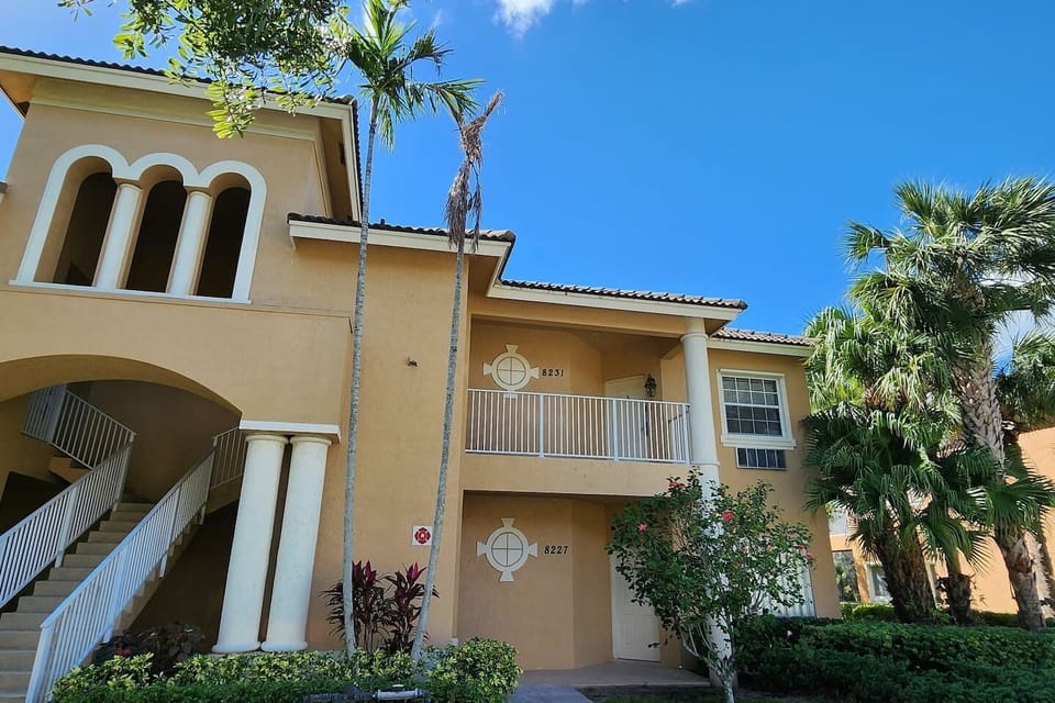 Exterior view of the building featuring tropical landscaping, covered entryways, and a bright Florida-style design.