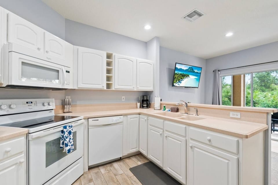 Bright kitchen with white cabinets, full-size appliances, breakfast bar, and an open view toward the living area.