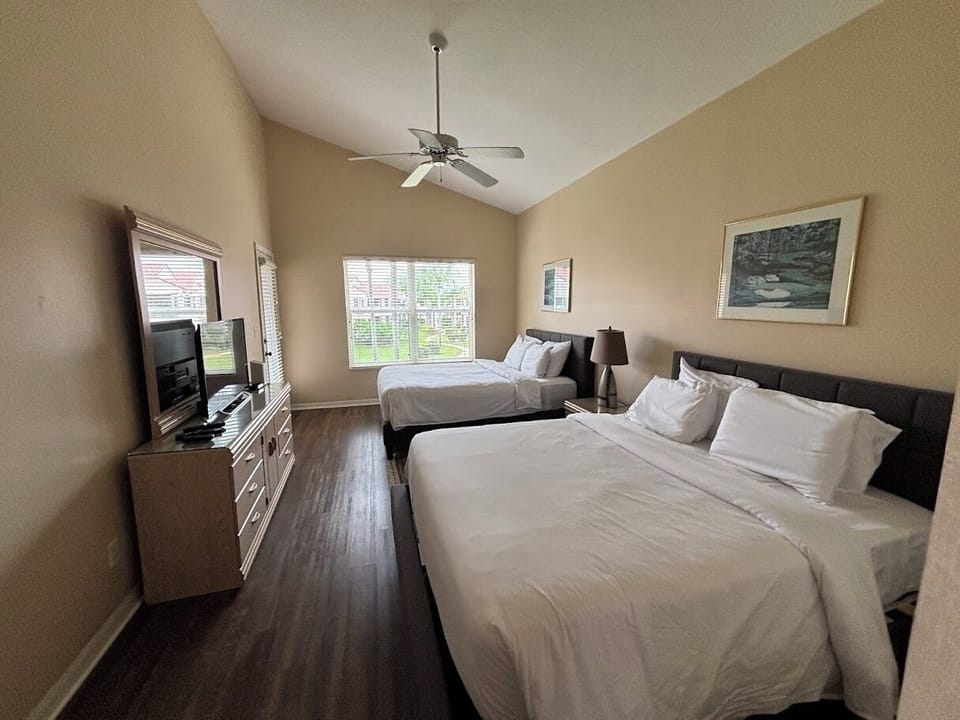 Comfortable bedroom with two beds, dresser storage, TV, wood-look flooring, and natural light.