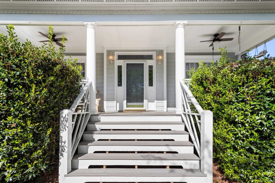 The wide front steps lead to a charming covered porch featuring classic white columns and cooling ceiling fans. It is a perfect spot for relaxing outdoors while enjoying the fresh air and neighborhood views.