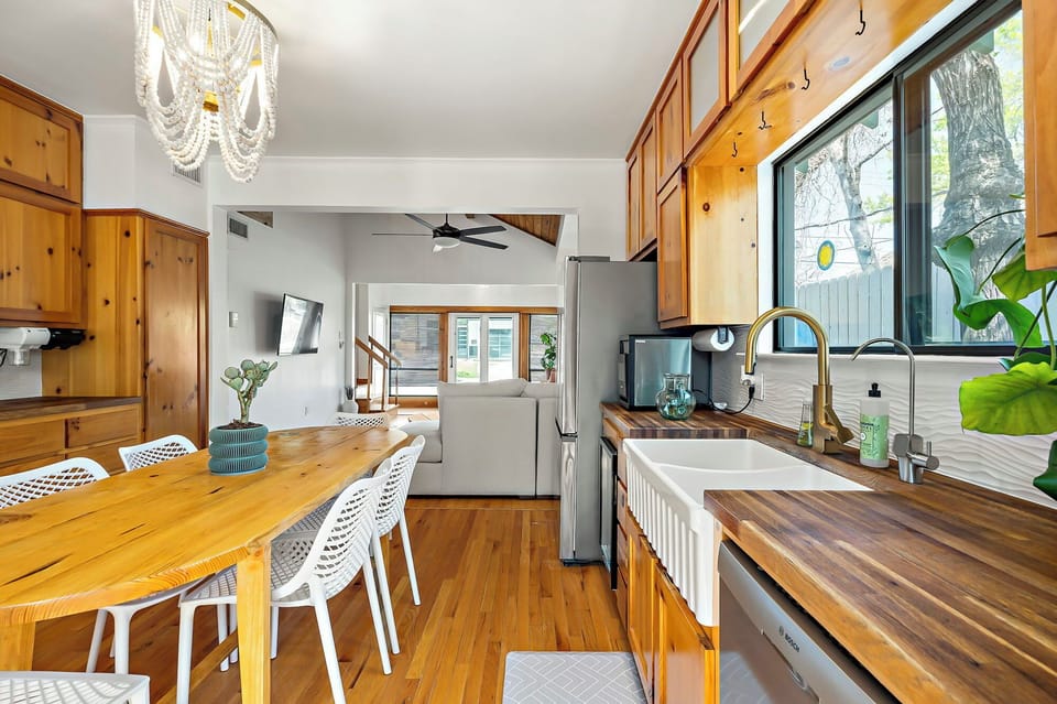 This well-lit kitchen and dining area features hardwood floors, wood cabinetry, and a spacious wooden dining table with white chairs.
