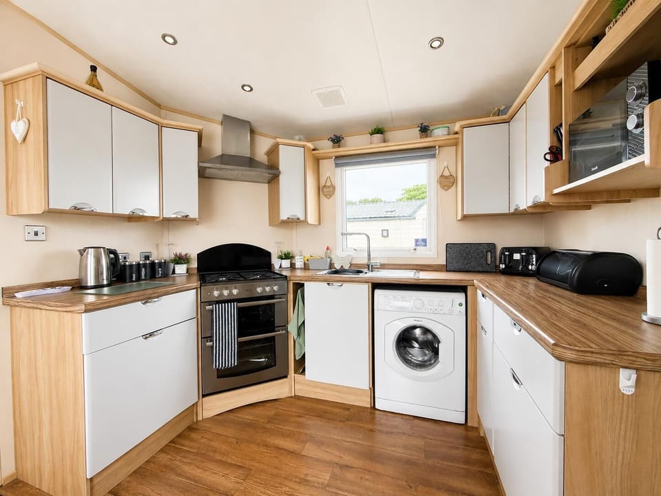 White and wood kitchen features a stainless steel oven, washing machine, microwave.