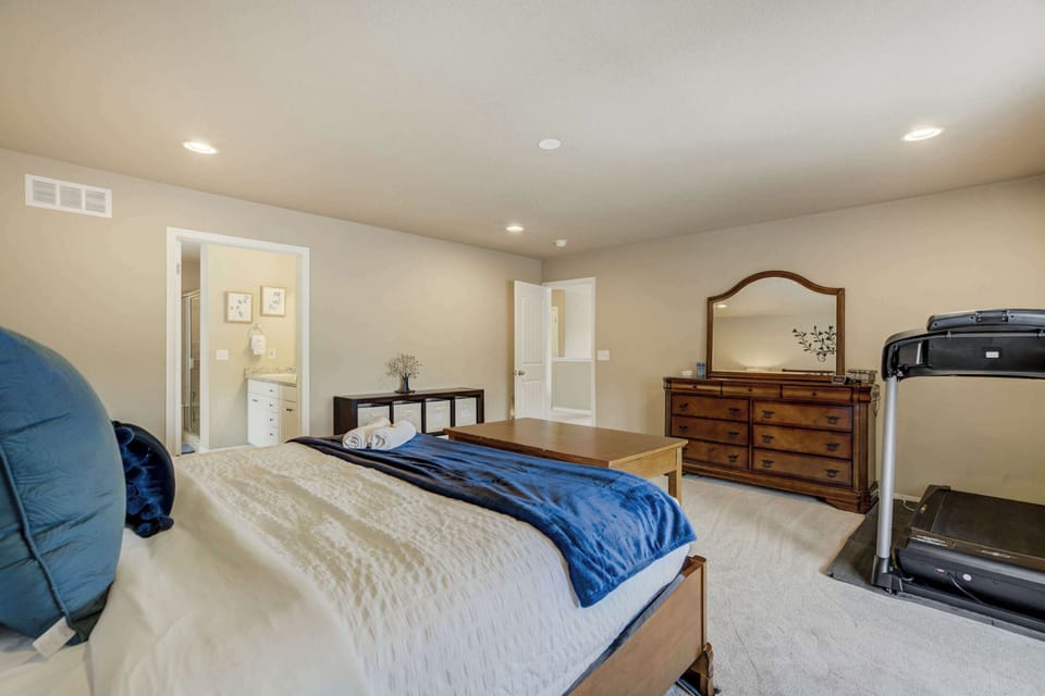 Expansive primary bedroom with a plush king-size bed, stylish furnishings, and large windows that fill the room with natural light. Includes a treadmill for staying active and a private ensuite bathroom for added convenience!