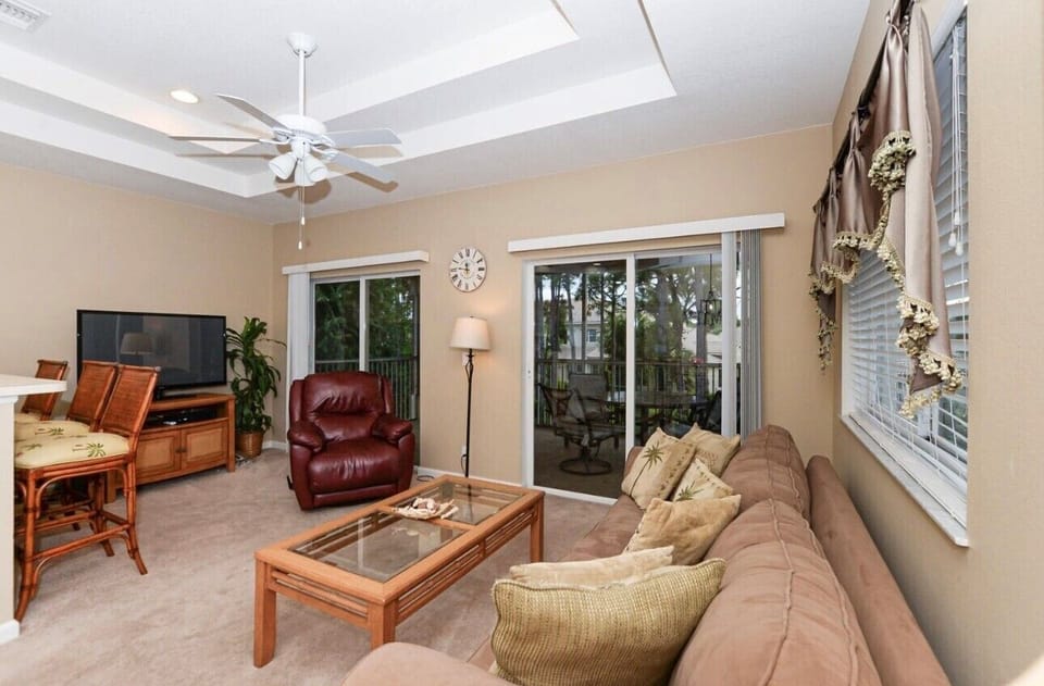 Comfortable living area with cozy seating, large windows, tile flooring, and direct access to the screened balcony.