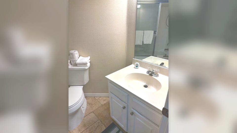 Bathroom with vanity storage, toilet, tile flooring, and bright mirror lighting.
