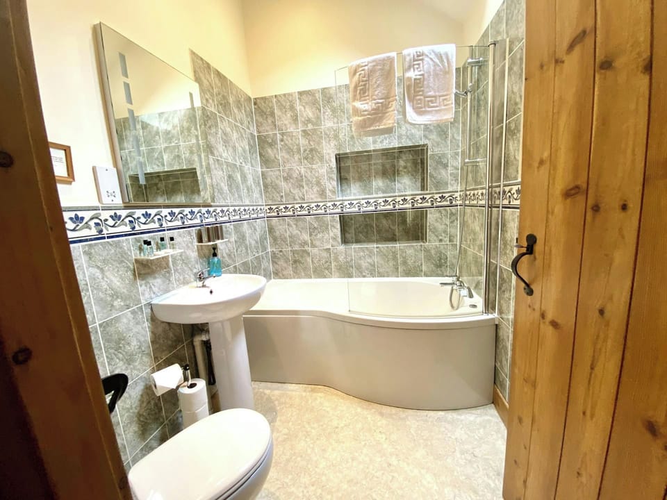 Tiled bathroom with pedestal sink, toilet and corner bath
