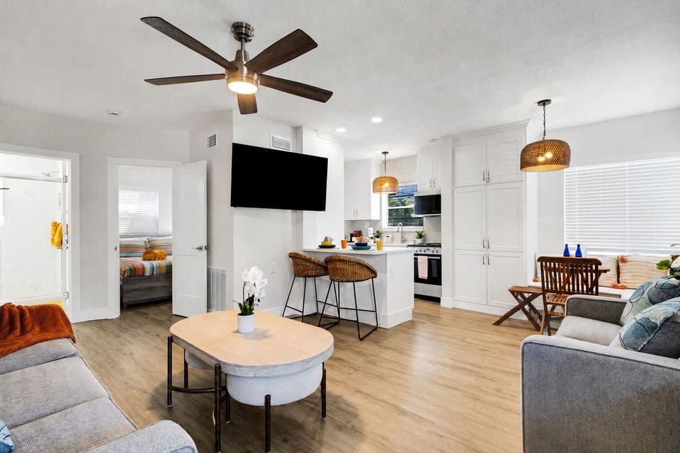 Bright, open-concept living area with plush seating, smart TV, and a cozy dining nook for four. Coastal decor and warm wood tones create a relaxed, beachy feel — the perfect spot to unwind after a day at the beach.