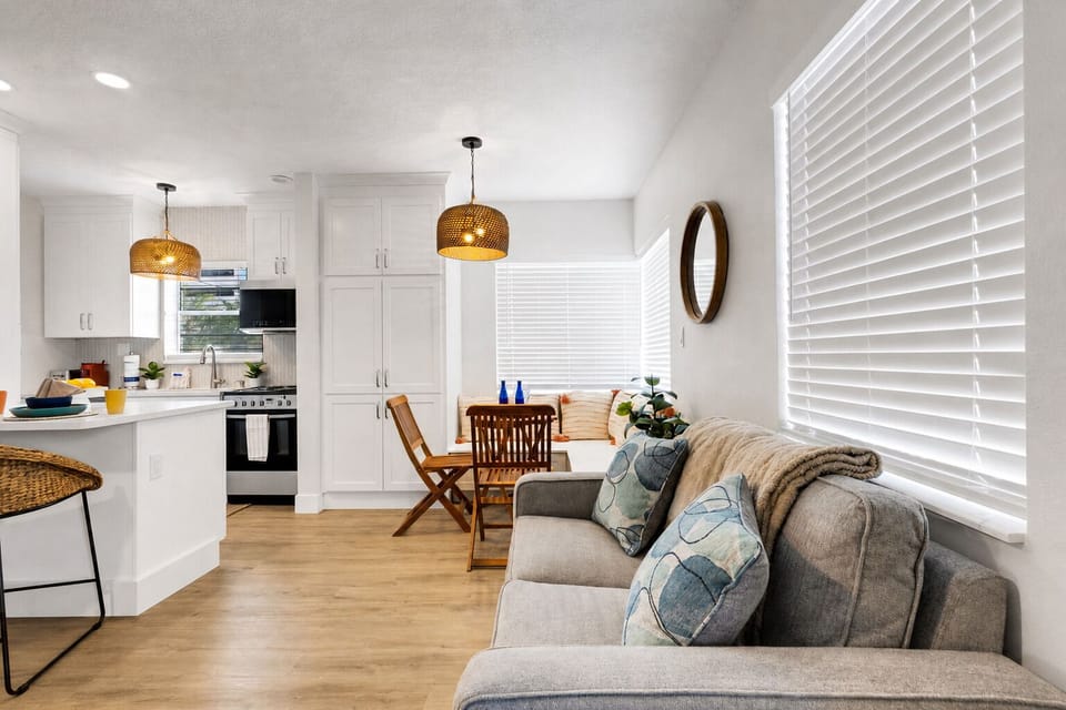 Bright, open-concept living area with plush seating, smart TV, and a cozy dining nook for four. Coastal decor and warm wood tones create a relaxed, beachy feel — the perfect spot to unwind after a day at the beach.