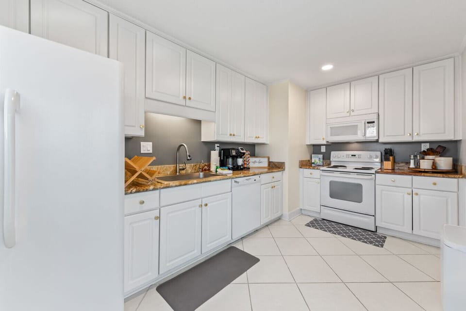The Seabreeze Villa kitchen is bright and welcoming, featuring crisp white cabinets, marble-inspired countertops, and gold accents. Equipped with modern essentials, including a coffee station to start your mornings right. ☕✨