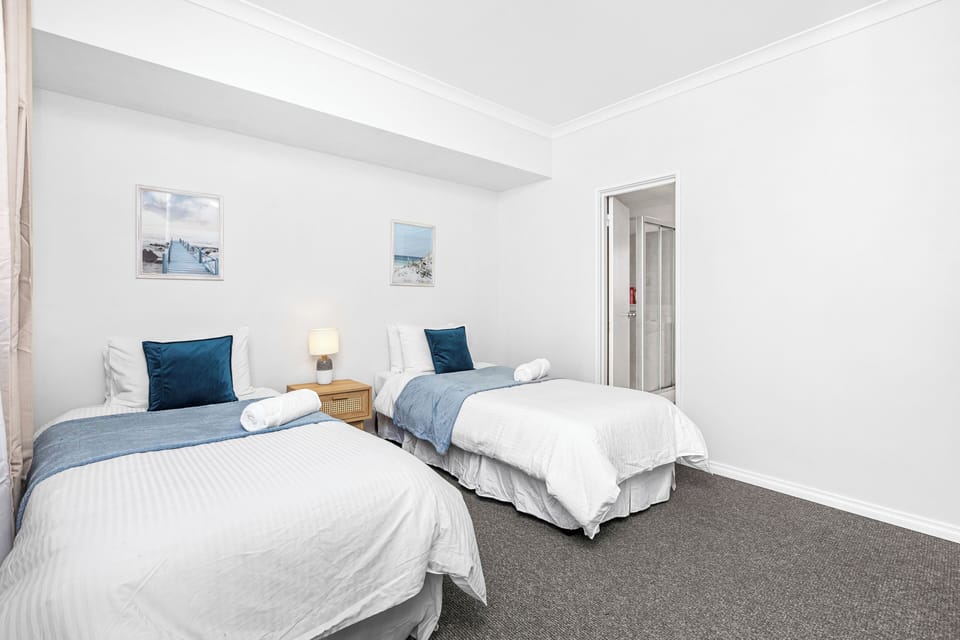 Rest comfortably in a clean twin bedroom with soft white linens, blue pillows, and simple, inviting decor.