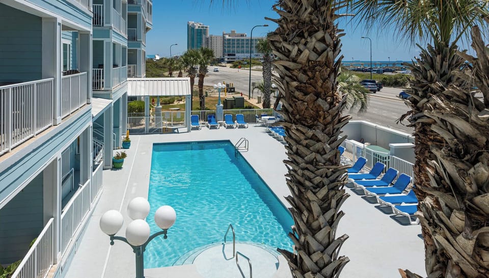 This inviting pool area features a sparkling blue pool surrounded by lounge chairs and palm trees, perfect for relaxation