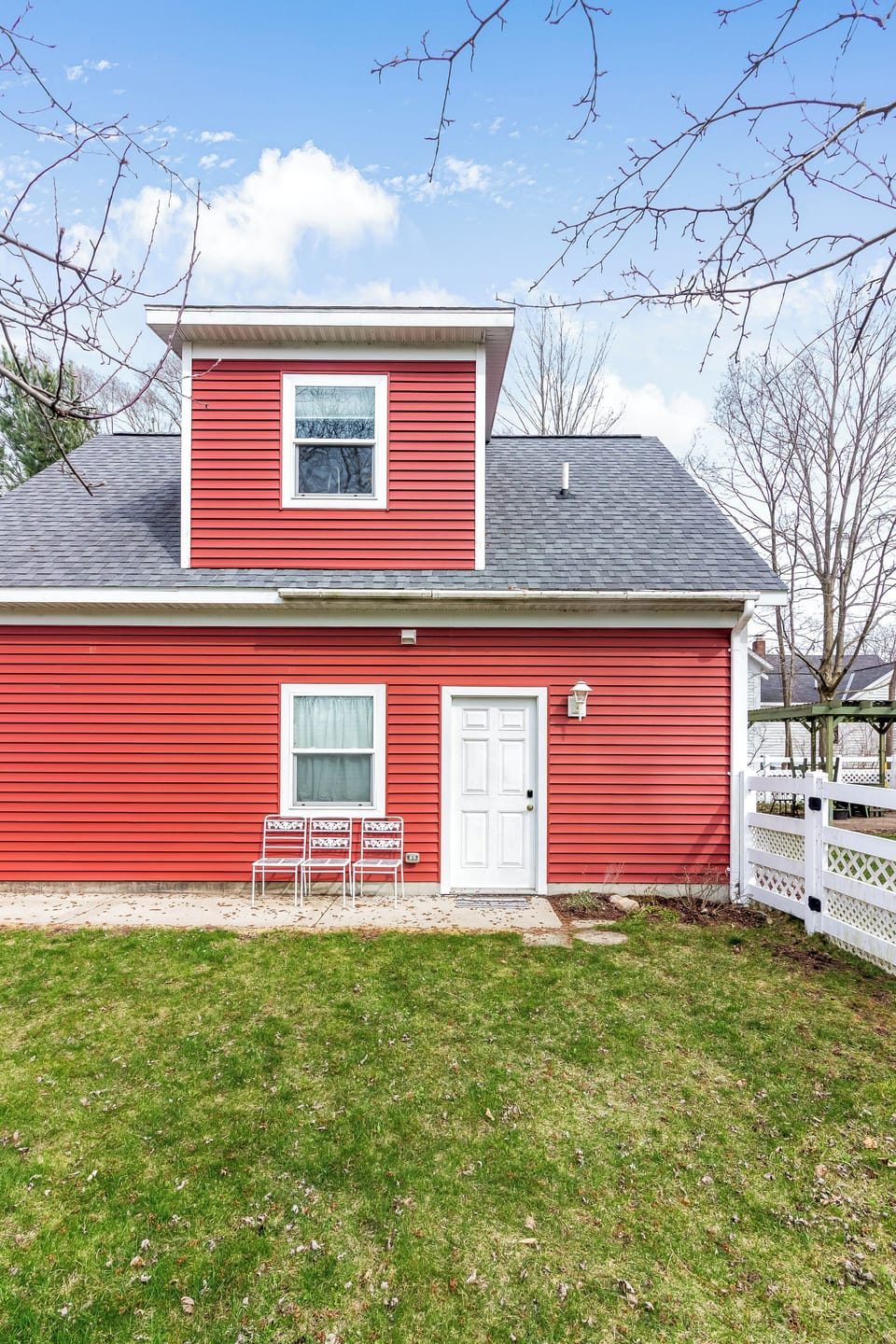 Red house with white trim, patio chairs, and grassy yard.








