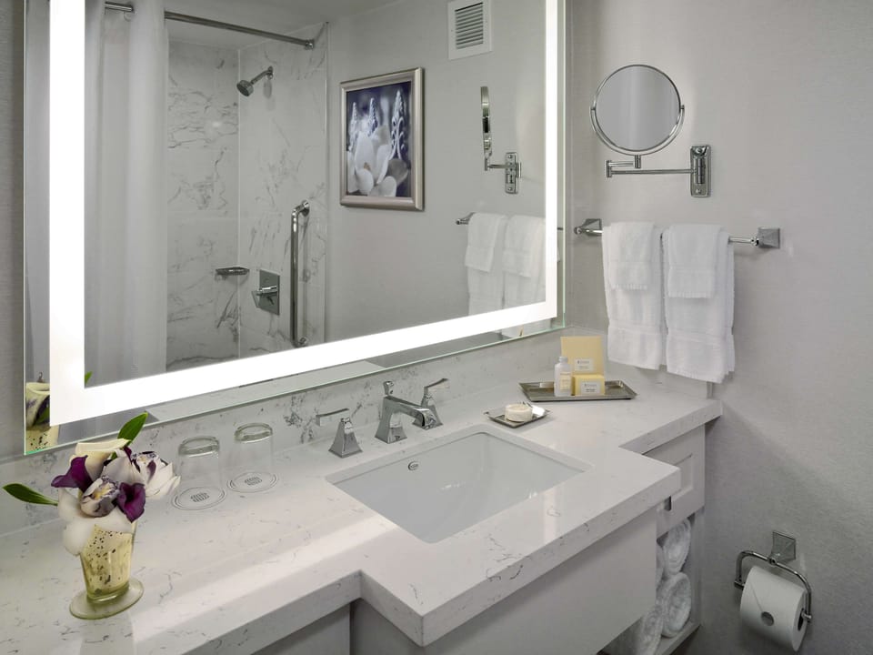 Refresh in a sleek marble bath with bright vanity mirror.